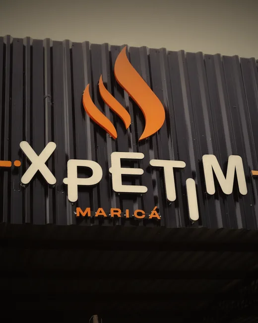 Letreiro Xpetim Maricá em letras brancas com a chama laranja sobre a fachada.