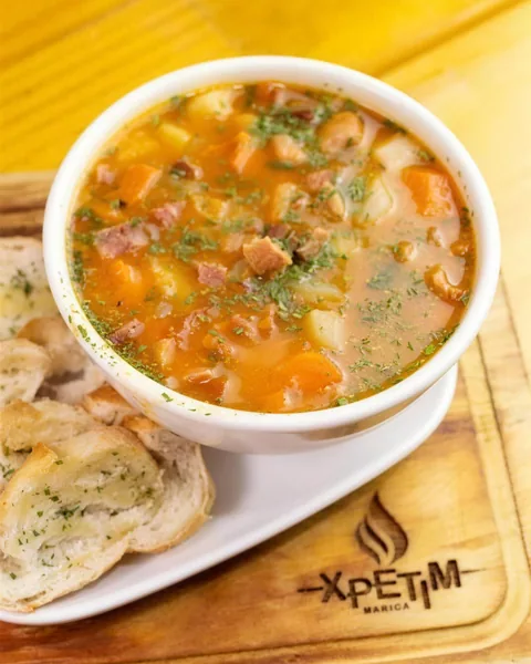 Caldo servido em cumbuca branca sobre tábua marcada Xpetim, com torradas ao lado.