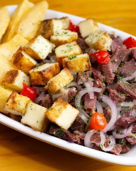 Porção de carne desfiada com cebola roxa, cubos de queijo coalho e mandioca frita.