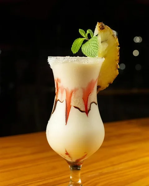 Drink cremoso em taça alta com raspas de chocolate, hortelã e fatia de abacaxi.